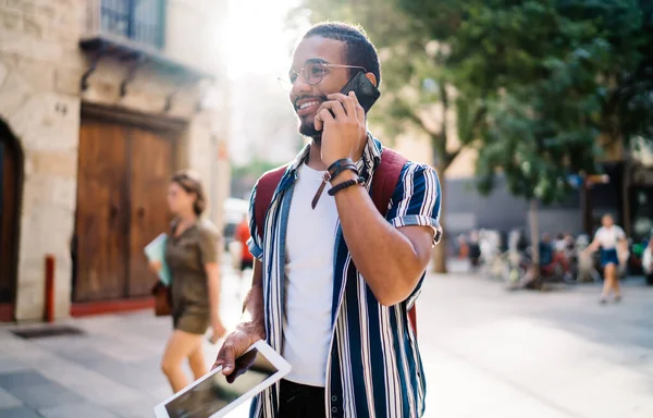 Positive young male traveler using roaming tarrifs making smartphone call visiting town on vacation holidays, smiling hipster guy tourist talking on mobile phone on international connection in travel