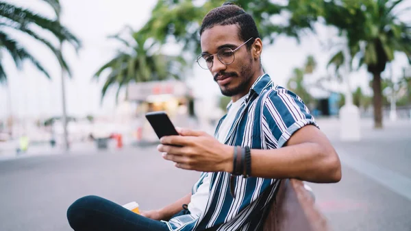 Chico Hipster Afroamericano Serio Recreándose Banco Sosteniendo Teléfono Móvil Para — Foto de Stock