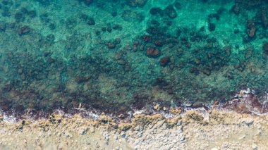 Üst katmanlı arkaplan görüntüsü gün ışığında altında küçük taşlar olan turkuaz okyanusun yakınındaki kuru, düzensiz, boş sahili temsil ediyor.