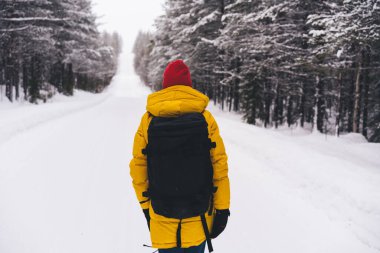 Norveç 'te soğuk bir kış günü, ağaçların yanındaki beyaz karlı yolda sırt çantalı, kimliği belirsiz birinin arka görüntüsü.