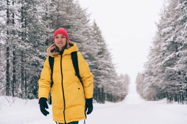 Norveç 'te soğuk bir kış günü, ormanın yakınındaki karlı yolda yürürken kılık kıyafetli, gülümseyen ve bakışlarını kaçıran mutlu kadın.