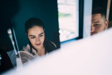 Camdan yüksek açılı genç profesyonel ofis çalışanları resmi kıyafetler giyip cam duvarın yanında duruyor ve birlikte yeni projeyi tartışıyorlar.