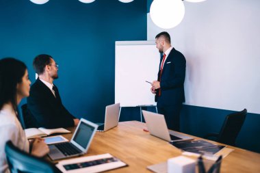 Takım elbiseli ve kravatlı zeki genç işadamlarının, brifing sırasında laptoplarla masada oturan çok ırklı meslektaşlarına projeyi açıklarken yan bakışları.