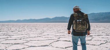 Dış görünüşü belirsiz bir erkek tuzlu bataklıkların ortasında bulutsuz gökyüzüne karşı duruyor.