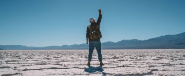 Arka planda şapkalı, kolları havada, güneşli bir günde Badwater havzasında dikilen kimliği belirsiz bir erkek görülüyor.