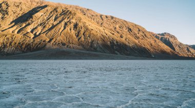 Göl kenarındaki dağlık arazide tuzla kaplı kuru yüzey, kötü su havzasında mavi gökyüzüne karşı.