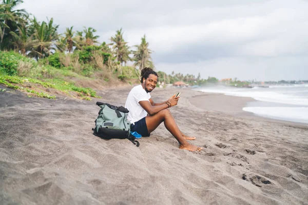 수염을 아프리카 미국인젊은 대낮에 스마트폰을 둘러보면서 해변에 카메라를 — 스톡 사진