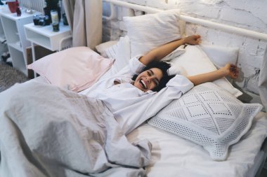 Pozitif pazar sabahı uyanırken uykusunda esneyen neşeli kadın, neşeli beyaz kadın hafta sonları tembel bir şekilde uyanıyor ve rahat yatak odasında dinleniyor.
