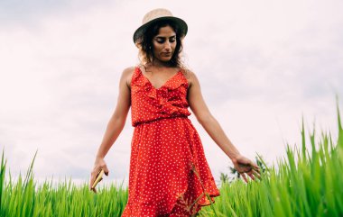 Şık şapkalı, parlak elbiseli, sakin genç bayandan yeşil çayırlarda gezinen ve bulutlu bir günde çimenlere dokunan
