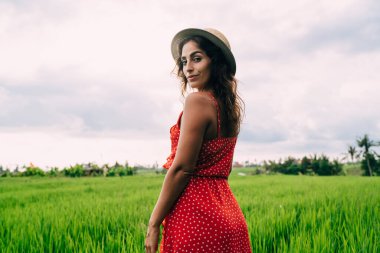 Haftasonu Bali 'de yeşil çayırlarda dinlenirken şık giyinmiş ince bir kadının kameraya bakışının yan görüntüsü.