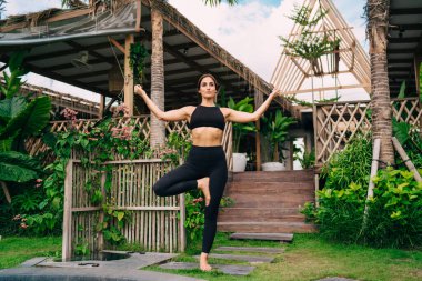 Siyah spor kıyafetleri giymiş güzel kadın yogi verandada meditasyon yaparken poz veriyor. İç huzuru bulmak ve ruh uyumunu sağlamak için çekici kadın dengeleri var. Sağlıklı yaşam tarzını korumak için.