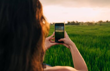Kadın blog yazarının Ubud 'daki Endonezya tatillerinde pirinç tarlalarını fotoğraflamak için cep telefonu teknolojisini kullanışının arka planı, hareketlilik için gezinen internete bağlanan video blogu çeken kadın