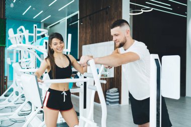 Hafif ferah spor salonunda erkek erkeğe spor yaparken modern spor aletlerine dokunurken gülümseyen pozitif kadın antrenör.
