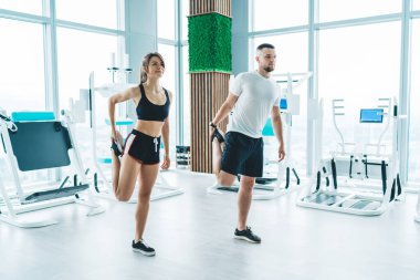 Spor yapan ve spor yapan bir çift modern spor salonunda spor makineleriyle antrenman yapmadan önce egzersiz yapıyor ve bacaklarını esnetiyor.