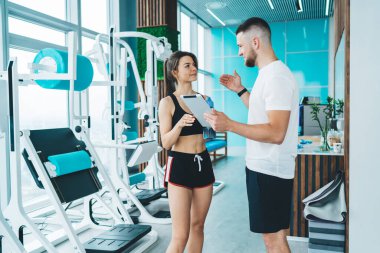 Çağdaş spor salonunda spor kıyafetleri içinde, spor kıyafetleri içinde modern egzersiz makinelerinin yanında duran sakallı eğitmenin yan görüntüsü.