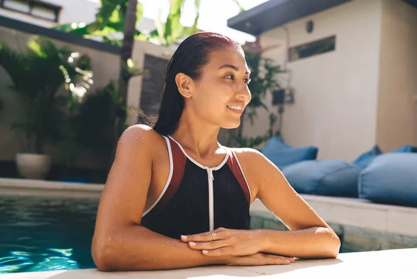 年轻漂亮的西班牙裔女士身穿黑色泳衣 在别墅后院里 靠着蓝色躺椅休息 眼睛朝外看去 — 图库照片