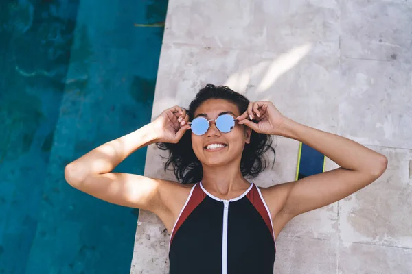在阳光明媚的夏日度假胜地 身穿泳衣 戴着太阳镜躺在游泳池边晒日光浴的年轻女性 — 图库照片