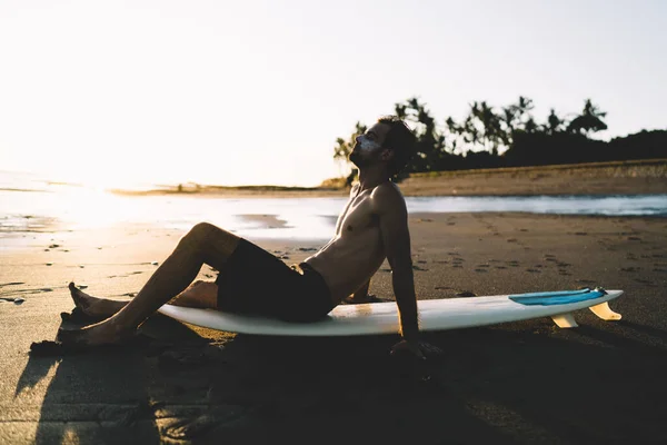 在黄昏时坐在沙滩上寻找灵感的男性专业冲浪板的侧视图 在夏季远航时在海洋边享受娱乐 — 图库照片