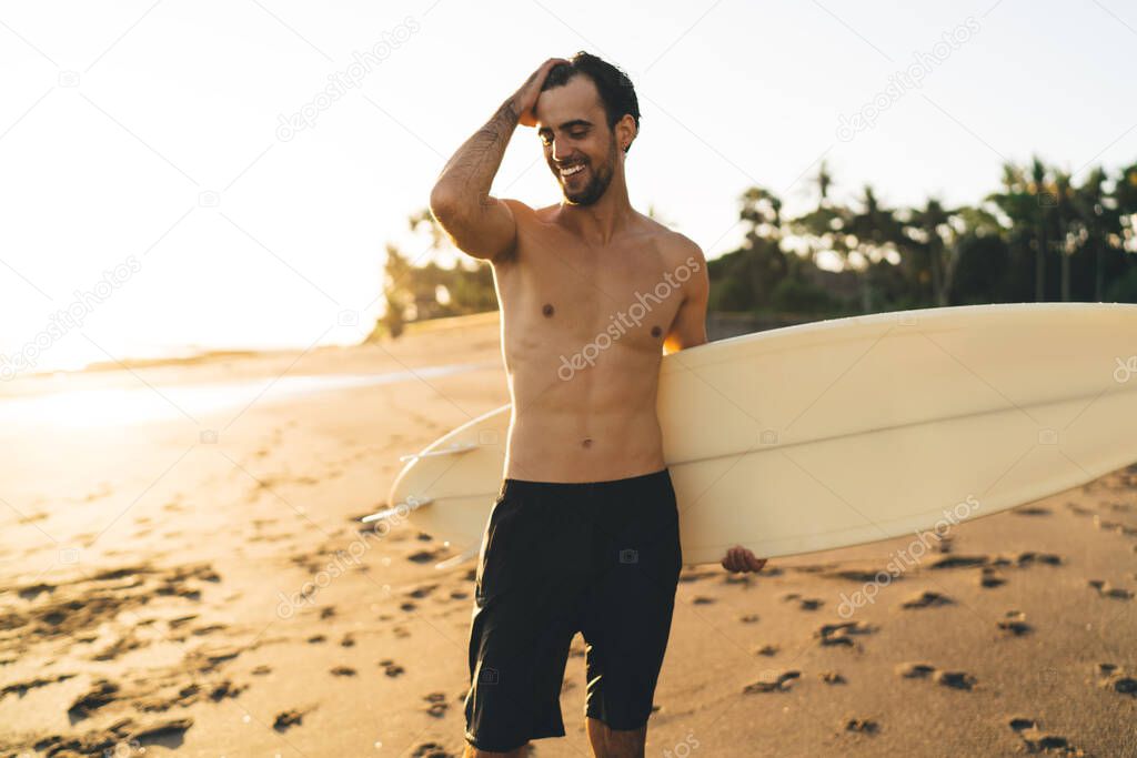 Cheerful surfer holding mock up surfboard with copy space for travel company or rent advertising, happy joyful guy enjoying summer tropical vacations for visiting Rio de Janeiro in Brazil