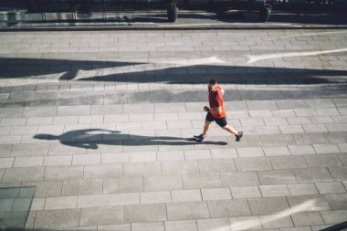 Yukarıdan bakıldığında spor ayakkabılı koşucunun güneşli bir günde kaldırımlı sokakta koşup bakışlarını kaçırdığı görülüyor.