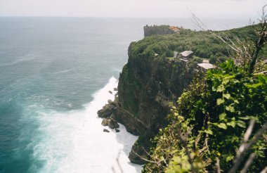 Yeşil kayalık dağ ve mavi dalgalı deniz ile yaz günü bulutlu gri gökyüzünün muhteşem manzarası.