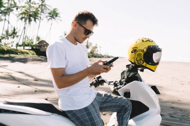 Güneşli havalarda motosikletin üzerinde otururken güneş gözlüğü ve güneş gözlüğü takan ciddi bir stil bisikletçisinin yan görüntüsü.