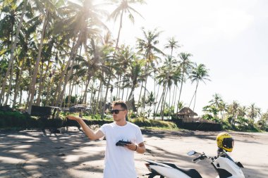 Uzaktan kumandalı havalı erkek turist seyahat sırasında kumsalda vakit geçirirken modern İHA 'yı elle yakalıyor.