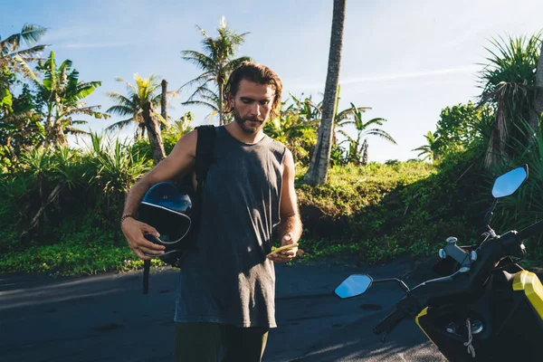Серьезный Бородатый Турист Шлемом Руке Стоящий Рядом Мотоциклом Серфинг Мобильный — стоковое фото
