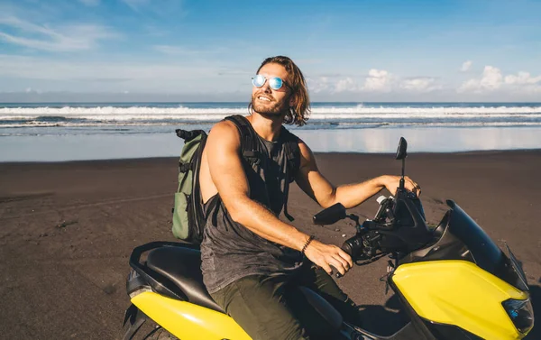 幸せな男性のヒップスターで バックパックは海の近くの自転車に座って 晴れた日を楽しみながら離れて見て ビーチで時間を過ごす — ストック写真