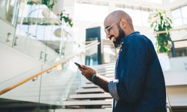 Elinde modern akıllı telefon cihazıyla gezen neşeli erkek kullanıcının yan görüntüsü 4G kablosuz internete bağlanıyor. Taşınabilirlik uygulaması üzerinden mesaj gönderen mutlu Orta Doğulu adam.