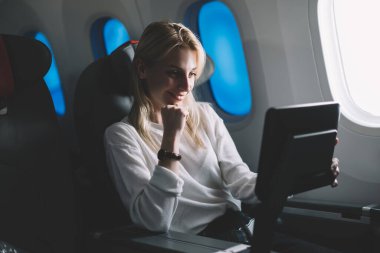 Rahat sarışın uçuş sırasında dinleniyor ve uçuş eğlence sisteminde televizyon izlerken gülümsüyor. 