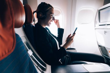 Resmi giyinmiş mutlu bayan yolcular, intercontinental uçuş sırasında intercontinental uçuşlarında interfifi bağlantısı olan, cep telefonu kullanan başarılı bir kadın tarafından gönderilen iyi haberle heyecanlanıyor.