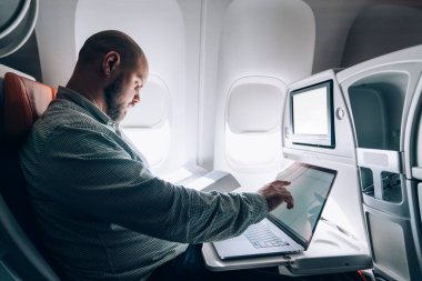 Ciddi bir erkeğin uçuş sırasında dinlenirken ve uçak penceresinin yanında otururken net kitap ekranına dokunup kitap okumasının yan görüntüsü.