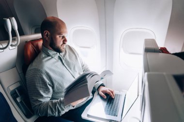 Yazar ve gazeteci ile uçuş sırasında iş toplantısından önce uçakta metin oluşturmak için edebiyat ve dizüstü bilgisayar uygulamaları tutan akıllı erkek kitap editörü