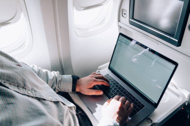 İnternette günlük kıyafetlerle dolaşan ve uçuş sırasında uçak penceresinin yanında otururken proje üzerinde çalışan çiftçi erkeğin üstünden.