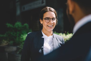 Katı siyah takım elbiseli neşeli gülümseyen genç bayan yazın şehir merkezinde iş arkadaşıyla konuşuyor.