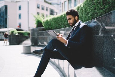 Odaklanmış iş adamı, siyah takım elbiseli beyaz gömlek kravatlı. Yazın şehirdeki granit bankta duran dosyaları kontrol ediyor.