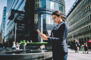 Resmi giyinmiş ve gözlüklü ciddi bir kadının, modern şehrin sokaklarında iş arkadaşıyla yaptığı telefon mesajlarıyla elde ettiği görüntüler.