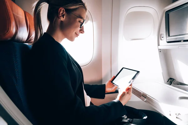 坐在飞机靠窗的地方 一边欣赏庄稼的侧面风景 一边欣赏优雅的女装和眼镜 一边阅读着平板电脑和飞机上令人毛骨悚然的电子书 — 图库照片