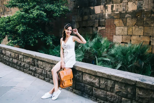 Vrolijke Reizende Vrouw Witte Overall Sneakers Zittend Hek Bewegend Haar — Stockfoto