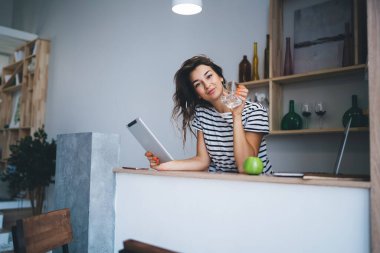 Kafkasyalı bir kadının yarım boy portresi kameraya bakıyor elinde tabletle mutfakta duruyor, hipster bir kız kameraya bakıyor dokunmatik ekranda yemek dağıtım servisini ayarlıyor.