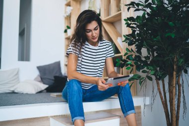 Düşünceli beyaz kadın dijital tablet kullanarak dijital tablet okuyarak dijital tablet kullanıyor. Modern apartmandaki kablosuz bağlantıyla tatmin olmuş bir kadın tabletle film izliyor.