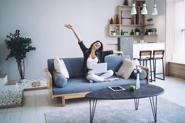 Happy caucasian female in eyewear feeling excited with completing online project working on freelance at home smiling woman looking at camera sitting on comfortable sofa with laptop computer