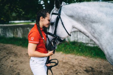 Hafta sonu at arkadaşlarıyla antrenman yapan kaygısız kadın jokeyin, safkan aygır kısrağına aşık beyaz jokeyin çiftlik arazisinde durup dinlenmesi.
