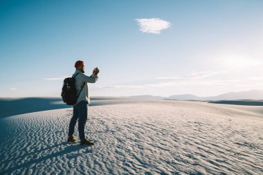 Beyaz tenli erkek nüfuz sahibi akıllı telefon kamerasıyla tatil sırasında beyaz çölün doğasını keşfediyor. Hipster adam seyahat blogu için cep telefonu kullanarak fotoğraf çekiyor.