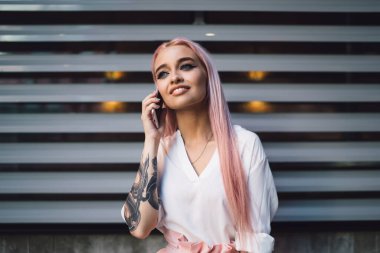 Dövmeli elleri ve renkli pembe saçları olan güzel bir kadın milenyumu kentsel tanıtım alanında duruyor ve uluslararası akıllı telefon konuşmaları yapıyor, şık hippi kız cep telefonuyla iletişim kuruyor.