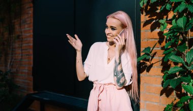 Beyaz dövmeli, pembe saçlı, pozitif uluslararası telefon görüşmesi sırasında gülümseyen hippi kız. İnternette en iyi arkadaşıyla sohbet ederken 4G 'ye bağlanan mutlu kadın.