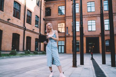 Elinde eğitim notları tutan mutlu beyaz okul öğrencisi kampüsün kenar mahallelerinde duruyor ve gülümsüyor, şık kotlar giymiş neşeli bayan öğrenci üniversite eğitimine ara vermenin keyfini çıkarıyor.