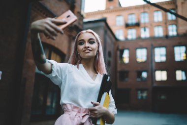 Ön kameraya gülümseyen beyaz kız öğrenci selfie fotoğraflarına tıklayarak mutlu hippi kız mesaj ve eskiz defteriyle medya resimlerine odaklanmak için cep telefonu uygulamasını kullanıyor.