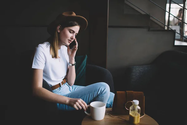 严肃的高加索女性千年 穿着时髦 头戴一顶帽子 坐在咖啡馆的内部 沉思的20多岁的嬉皮士女孩在闲暇时用智能手机打电话聊天 — 图库照片